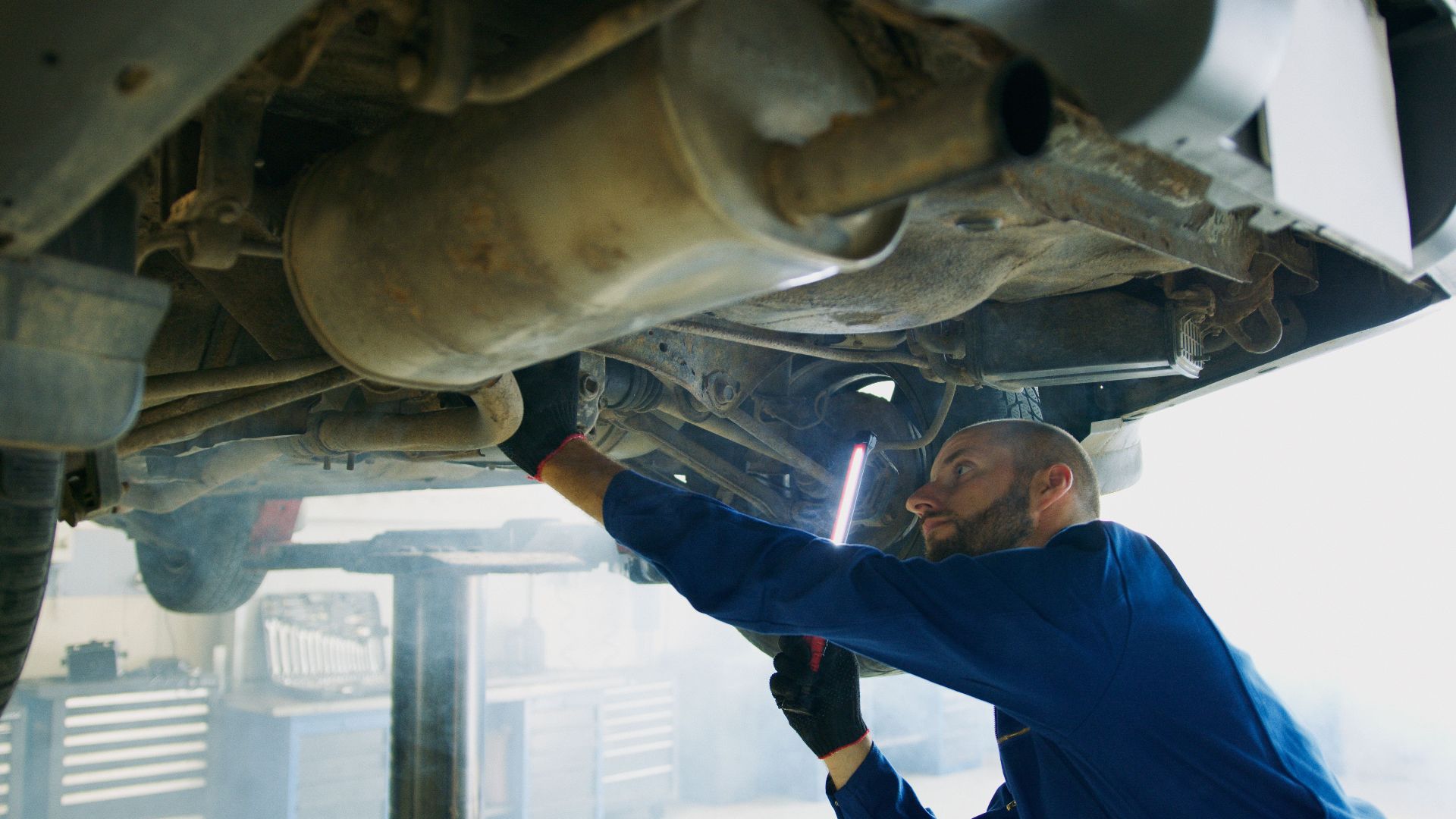 Skilled mechanic performing thorough maintenance under a vehicle in a professional garage setting.
