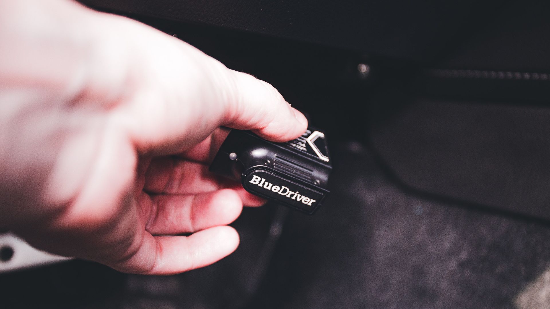 Close-up of a hand connecting a BlueDriver diagnostic device in a vehicle. Ideal for automotive and technology themes.