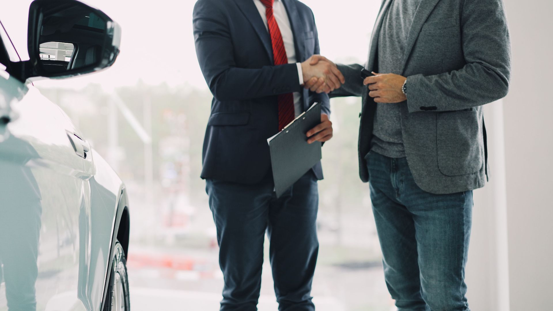 Two men shake hands in a car dealership, sealing a business deal.