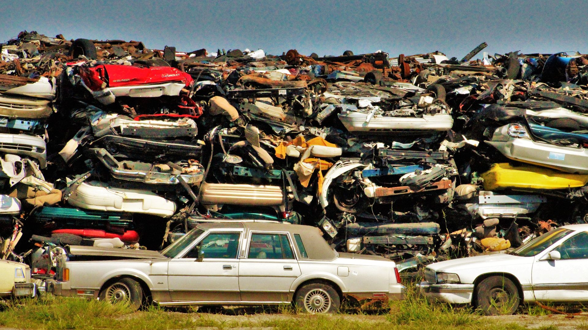 A large stack of disposed vehicles in an outdoor junkyard.