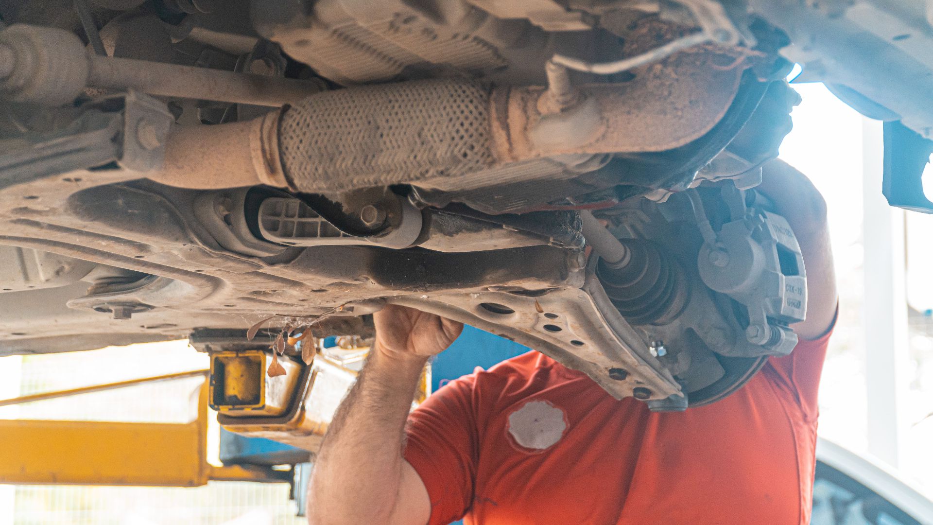 Mechanic working under a vehicle, inspecting the undercarriage in a repair garage, ensuring safety and performance.