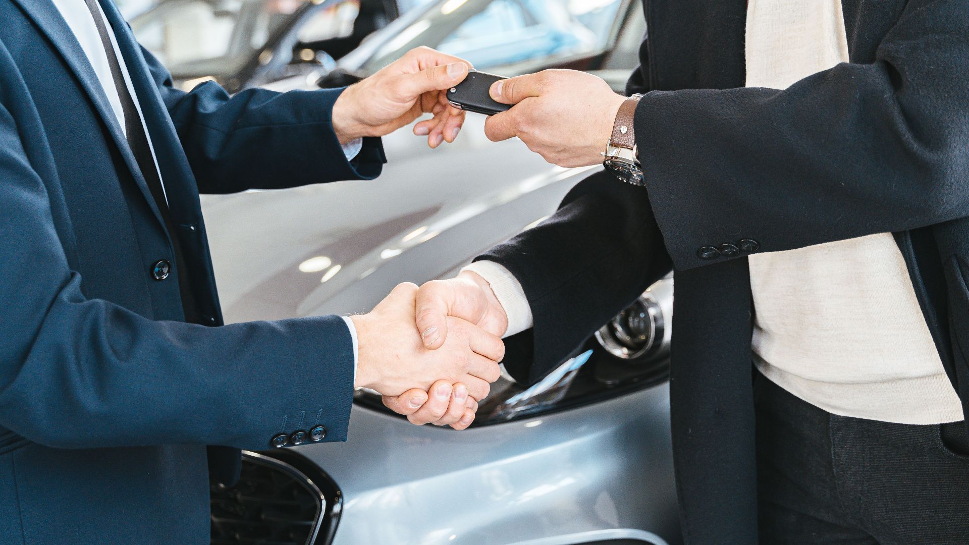 Two businessmen shaking hands and exchanging car keys in a dealership. Symbolizes a successful deal.