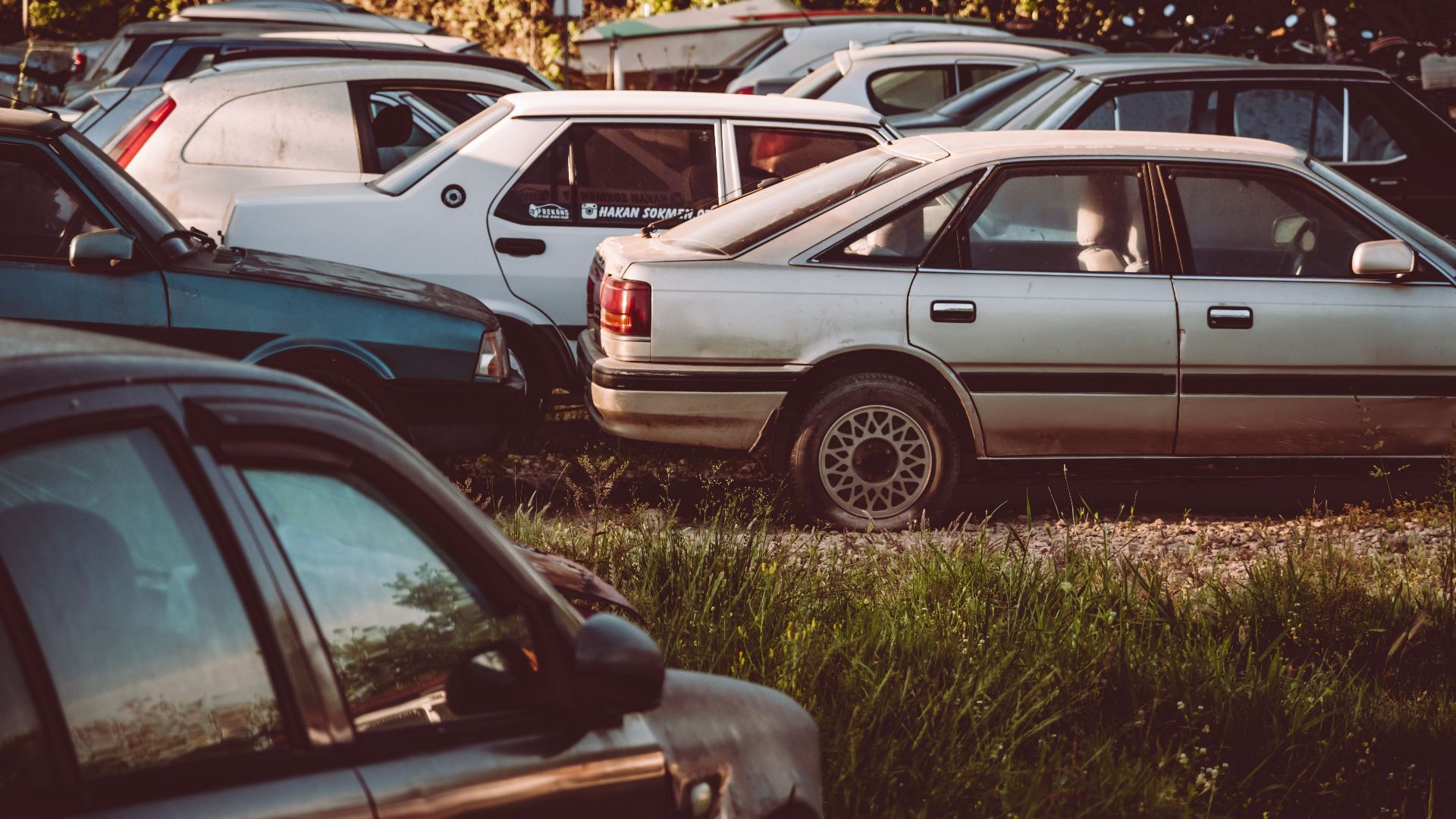 A collection of abandoned, rusting cars in an overgrown field, capturing a vintage feel.