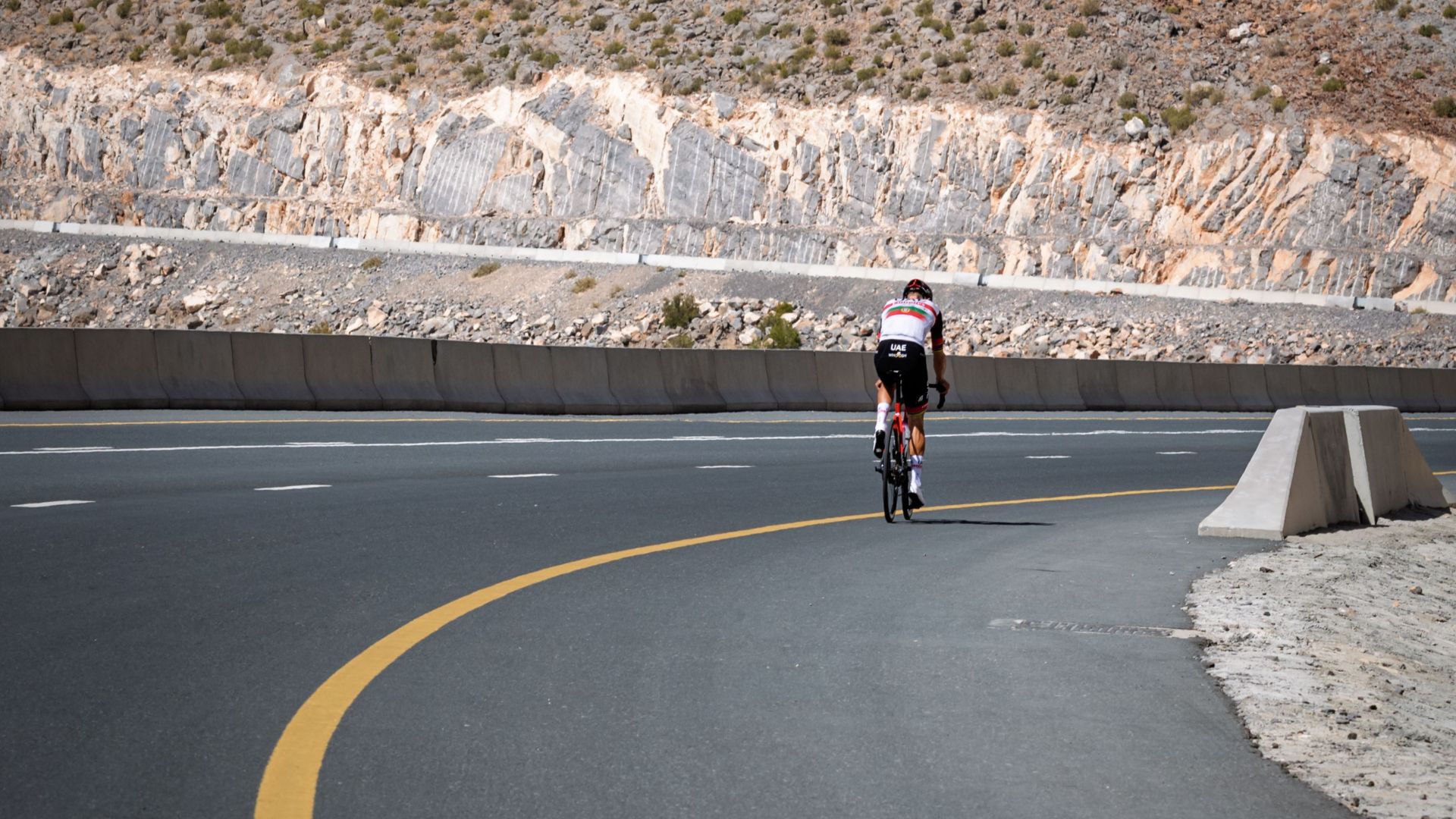 A lone cyclist riding on a winding mountain road under clear blue skies.