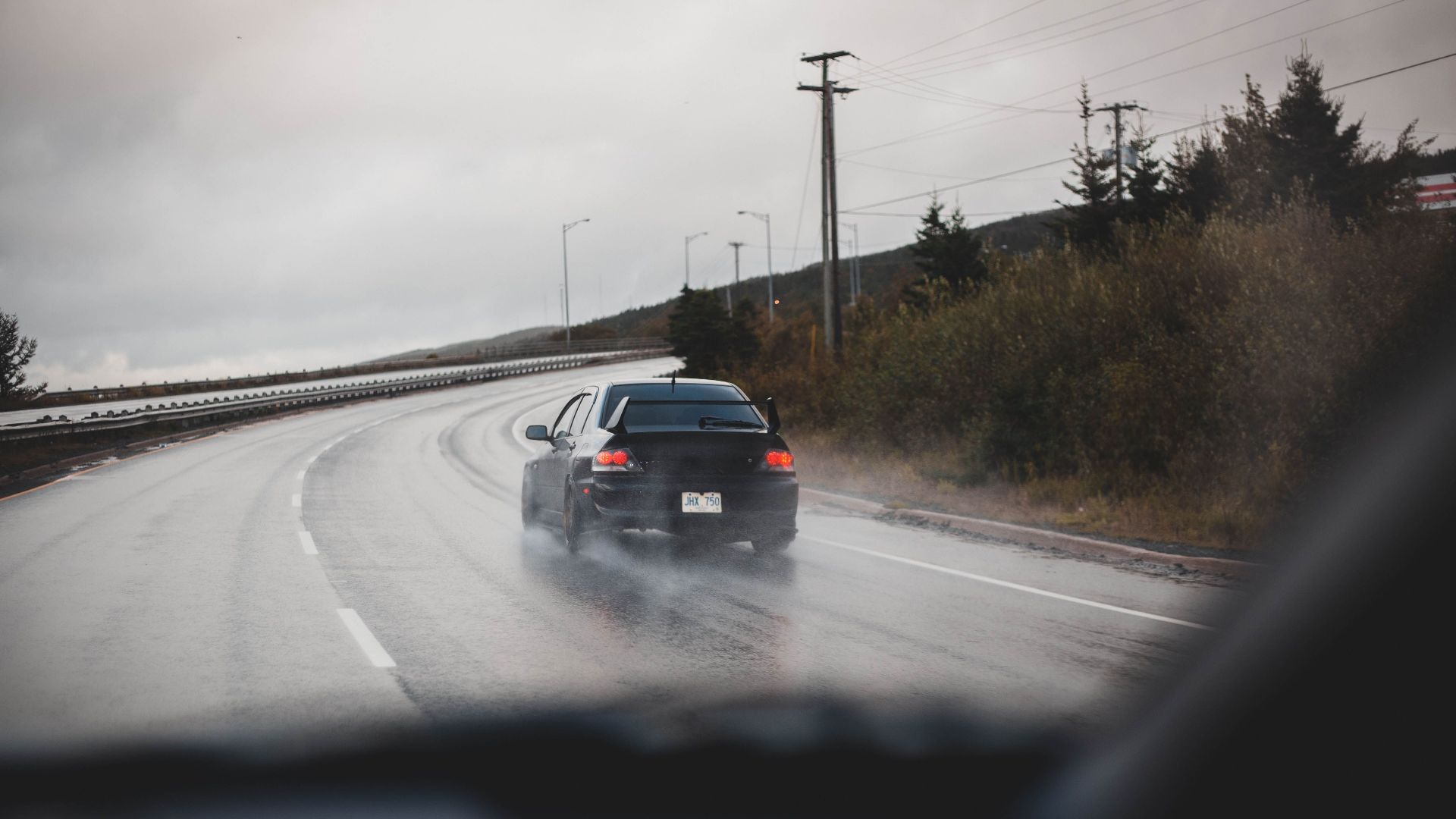 A black car drives on a rainy highway, showcasing speed and transportation.