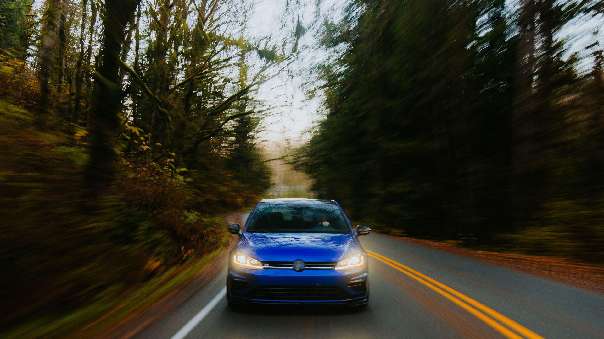 Dynamic shot of a blue car speeding through a forest road.
