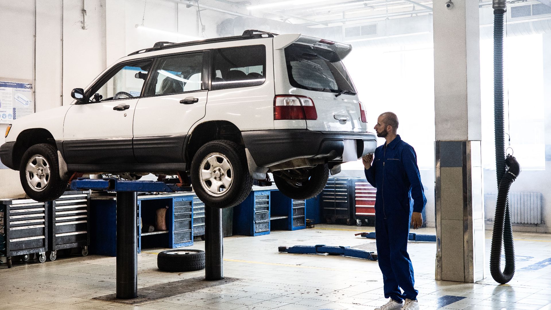 Mechanic inspecting a lifted SUV in a modern auto repair garage.