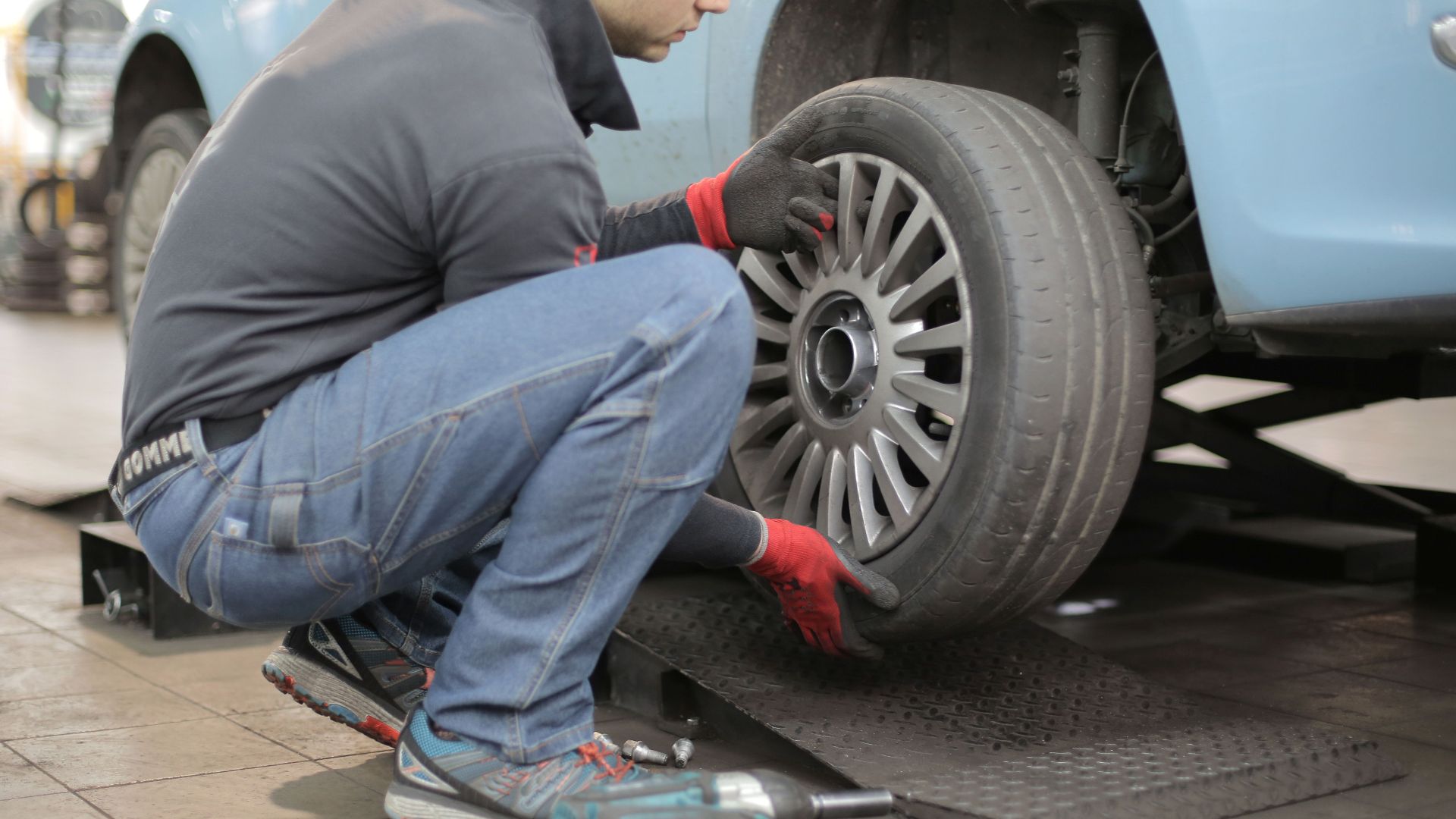 Mechanic changing a car tire indoors, using tools for vehicle maintenance.