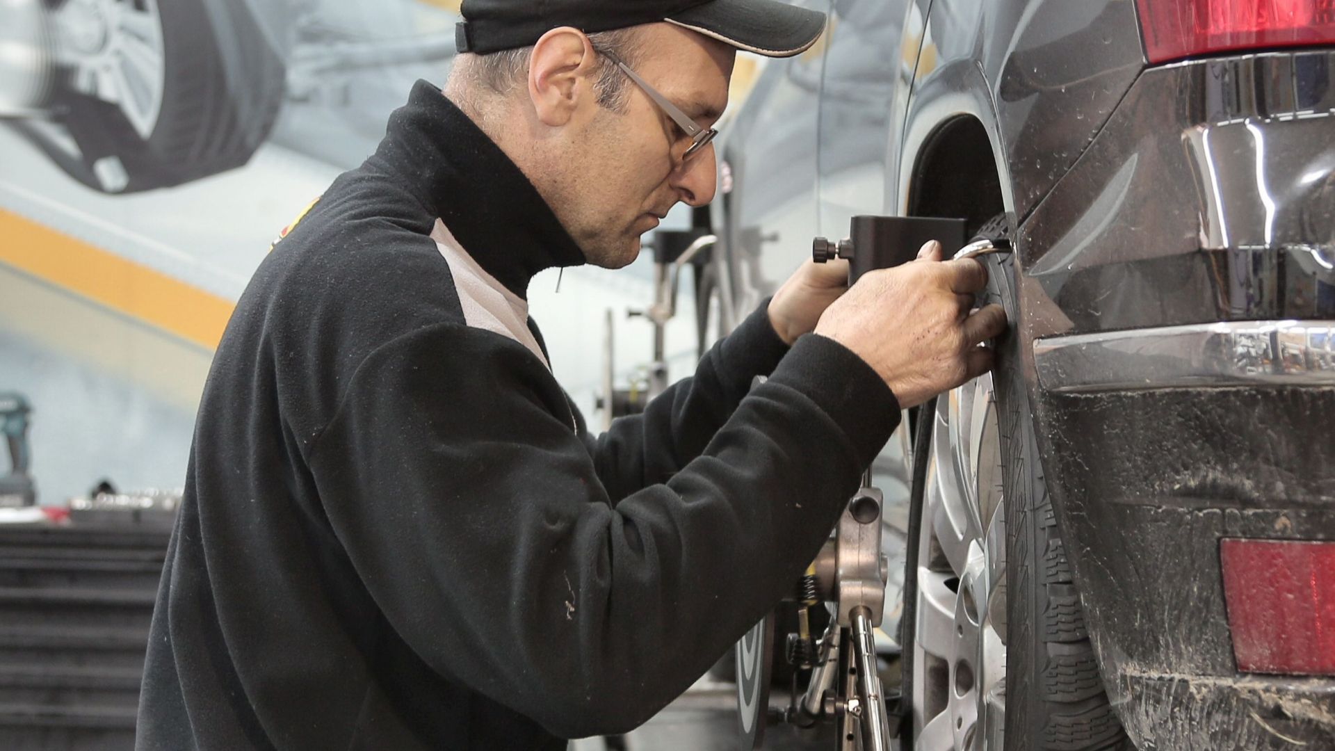 Side view of a mechanic aligning a car tire in a professional auto workshop.