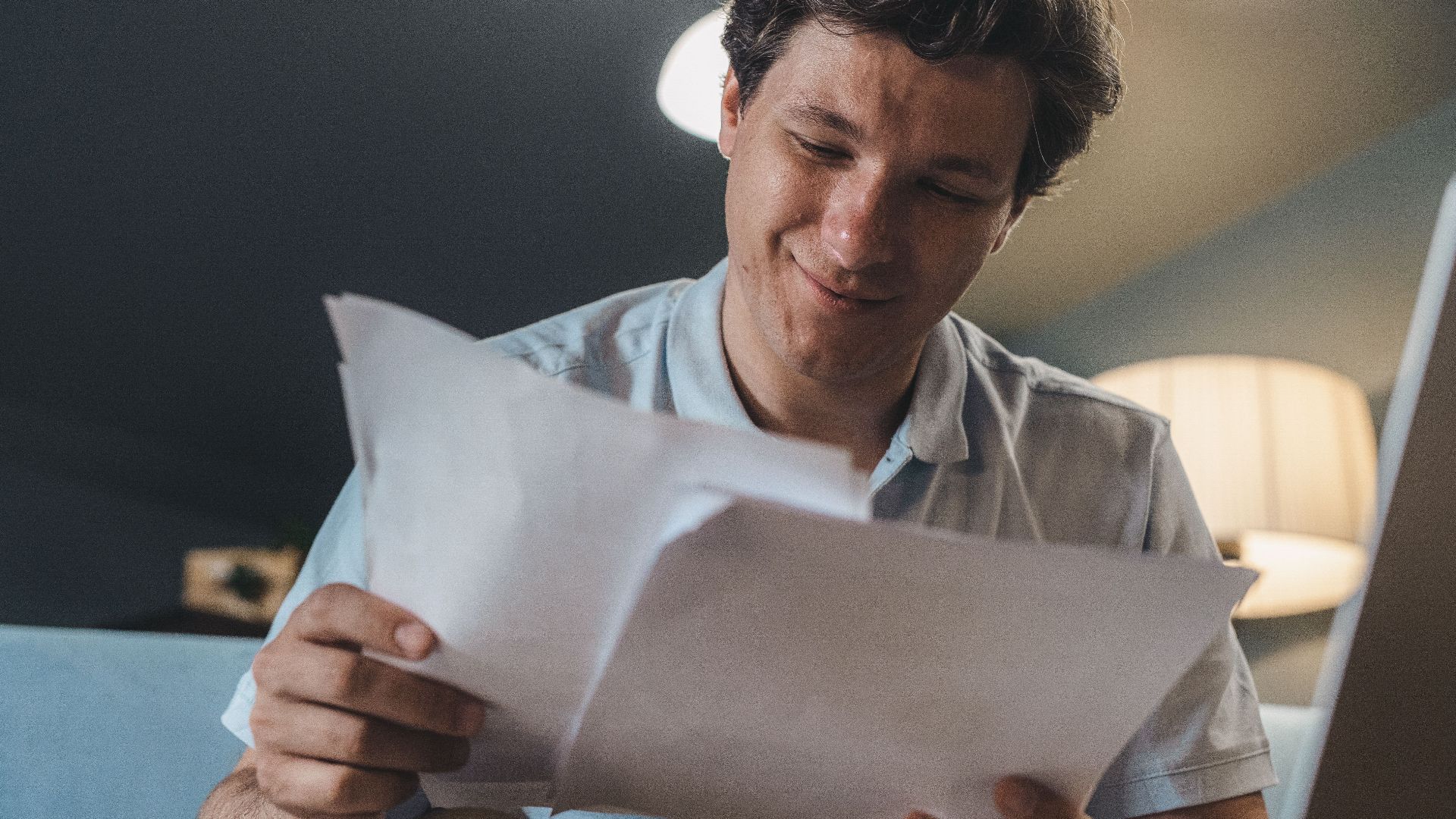 A cheerful man reading papers in a cozy indoor setting, radiating positivity.