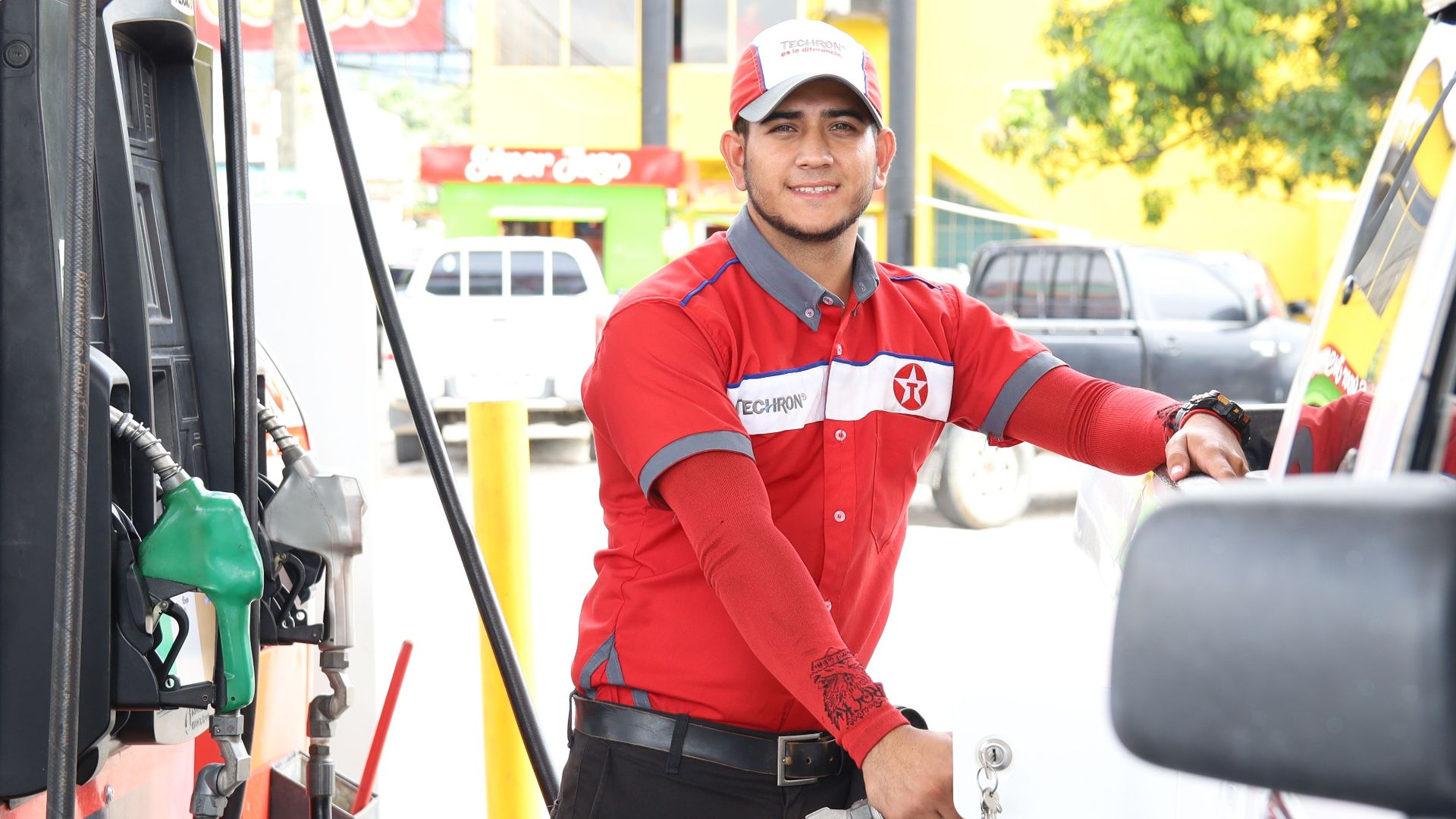 Cheerful gas station attendant refueling a car during the day.