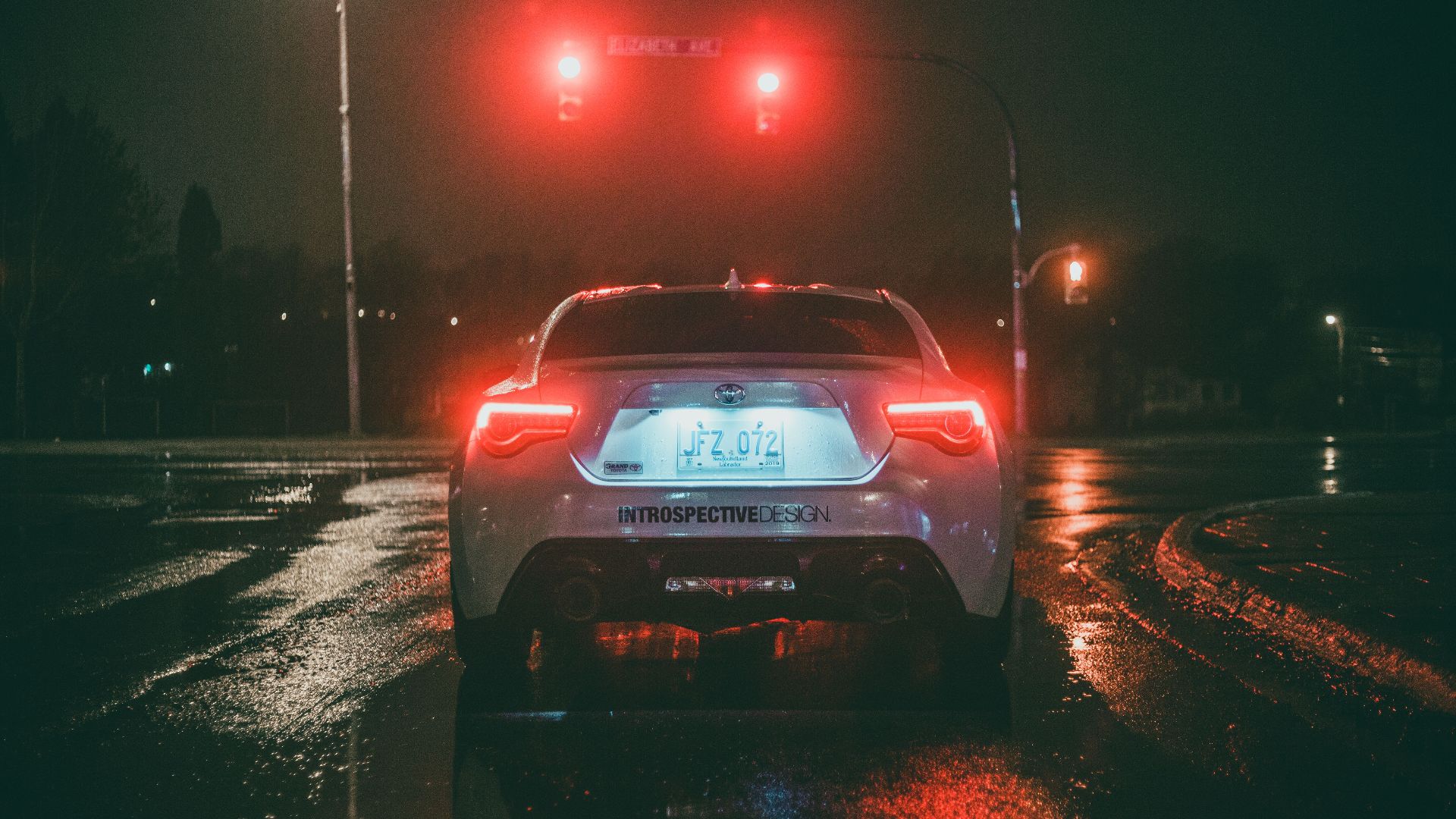 A car waits at a red light on a wet city street at night, capturing urban nightlife.