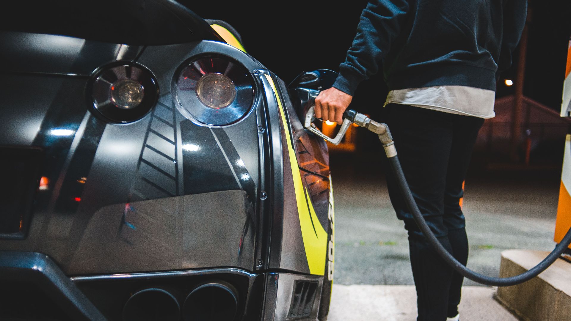Side view of crop unrecognizable male refueling modern racing automobile in petrol station in evening