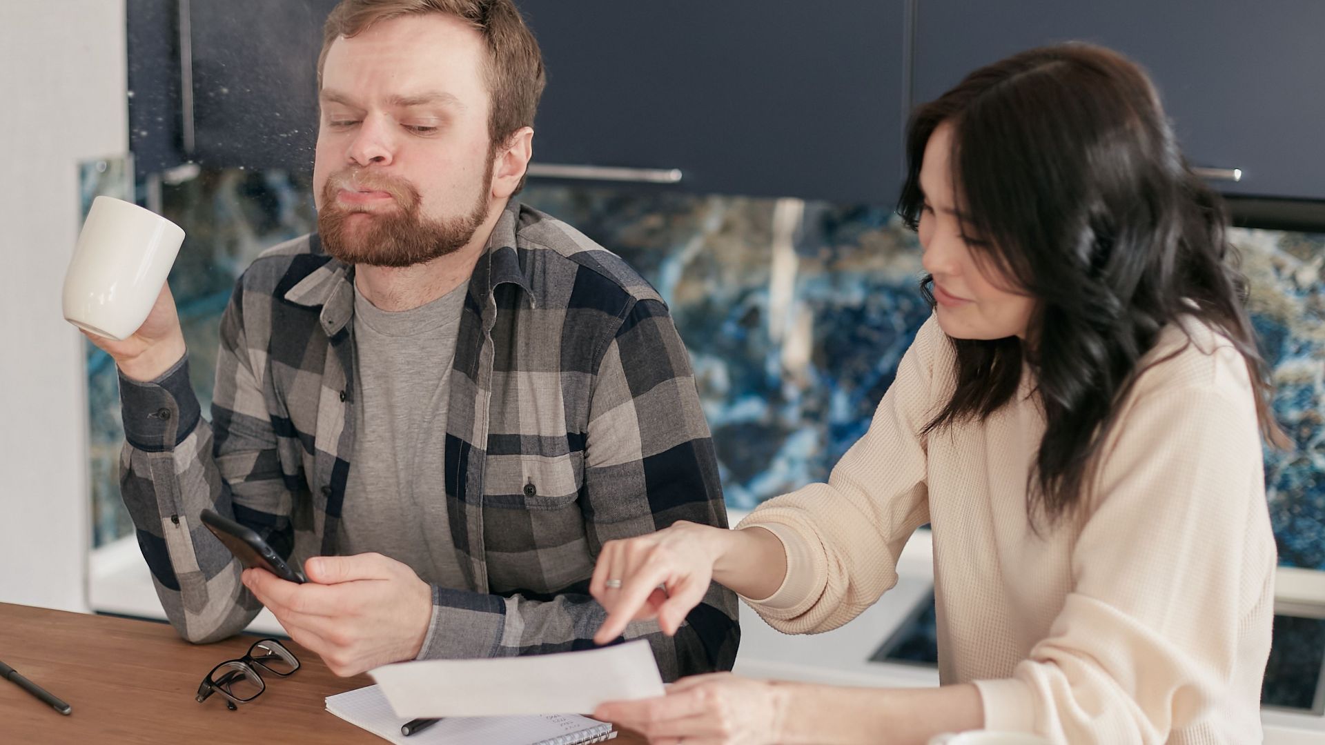 A couple reviews bills at their kitchen table, looking concerned and thoughtful.