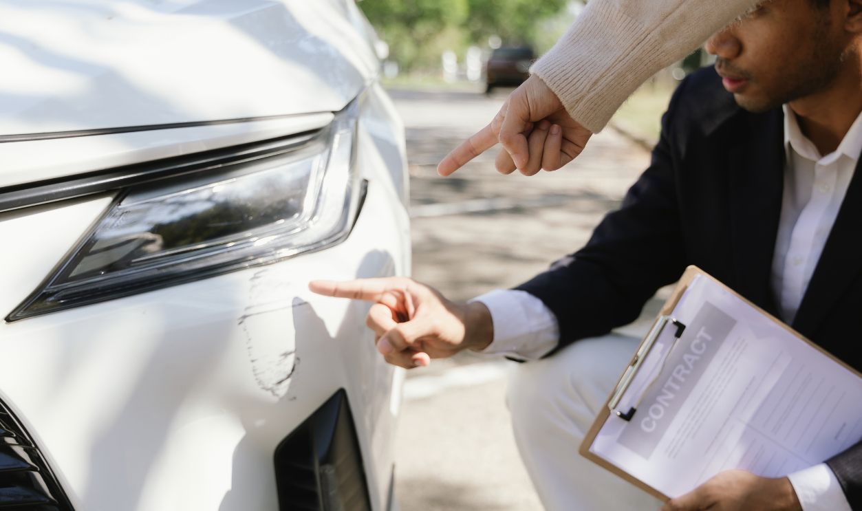 Insurance agents assist clients in an outdoor setting after a car accident, inspecting the vehicle for damage, discussing policy coverage, repair options, liability, and pursuing a claim. 