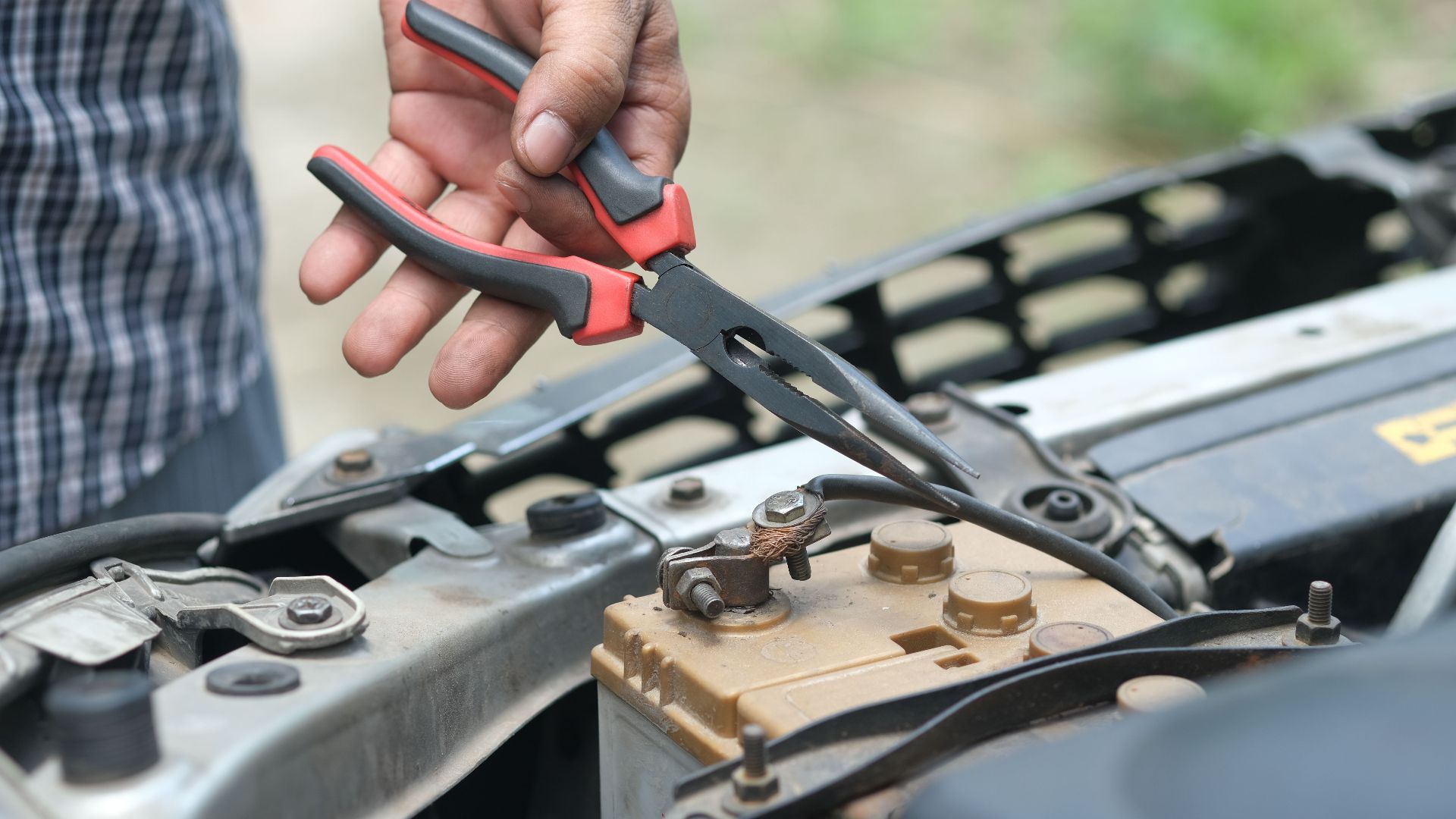 Person using pliers to check a car battery in an outdoor setting.