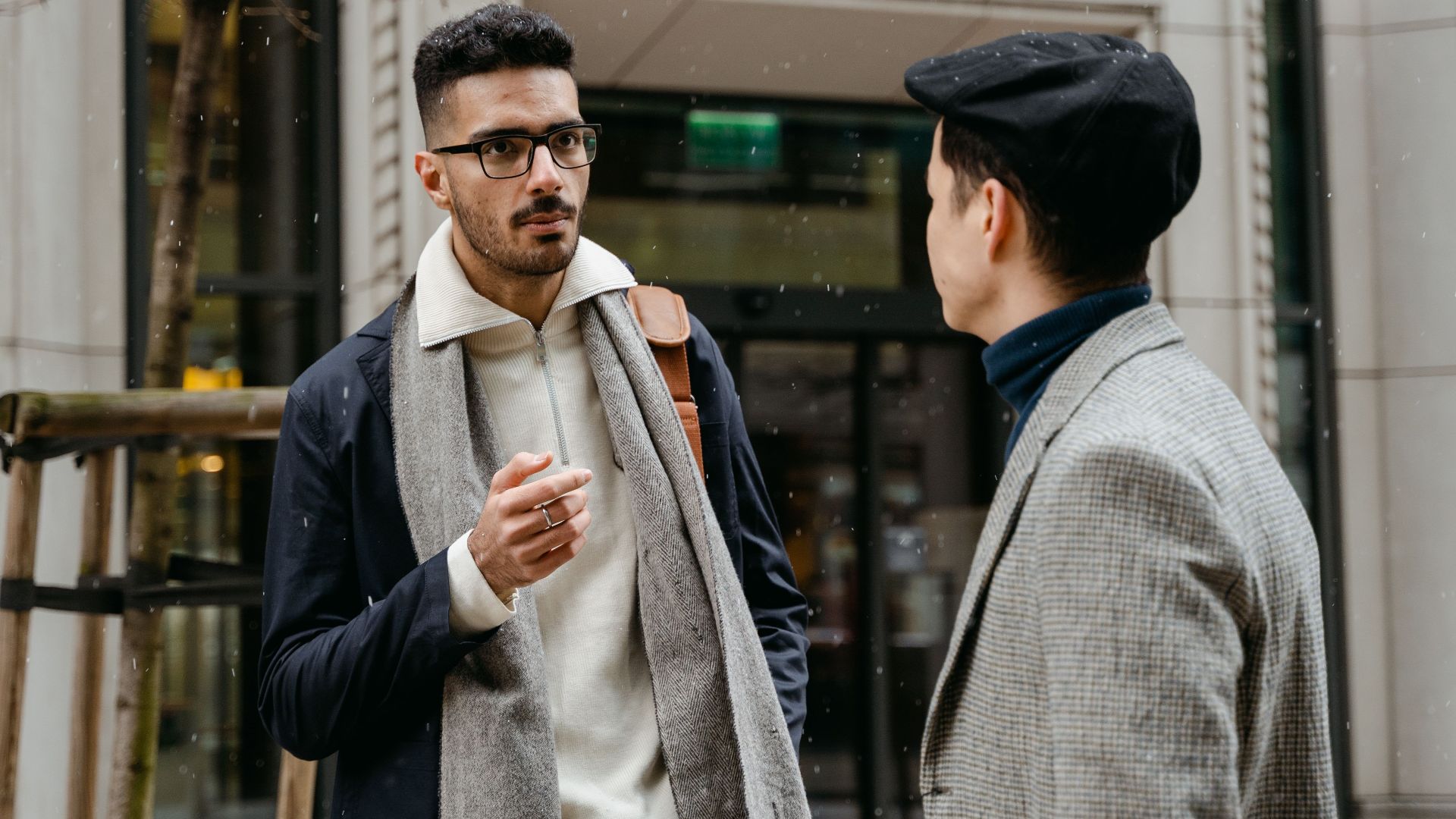 Two businessmen engaged in conversation outside in winter attire with snow falling lightly.