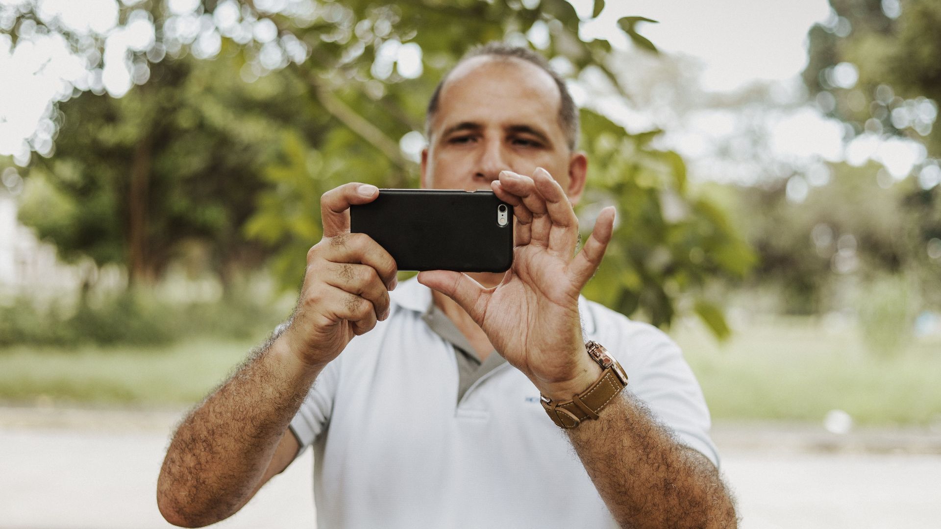 Adult man using smartphone to take a photo in a natural setting, showcasing modern technology and leisure.