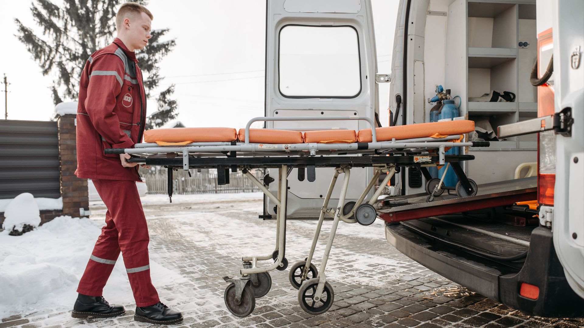 A paramedic loads a stretcher into an ambulance on a snowy day, showcasing emergency response readiness.