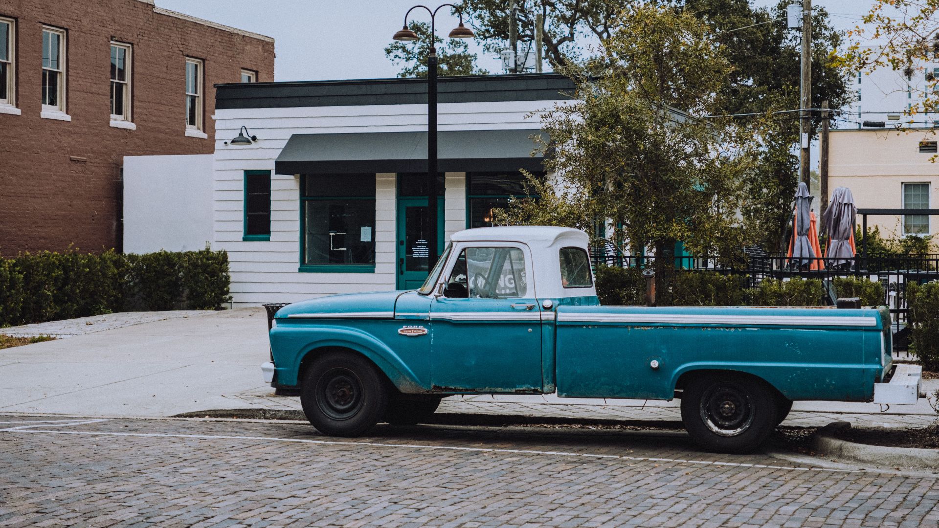A classic blue Ford truck parked on a cobblestone street in a quaint urban area.