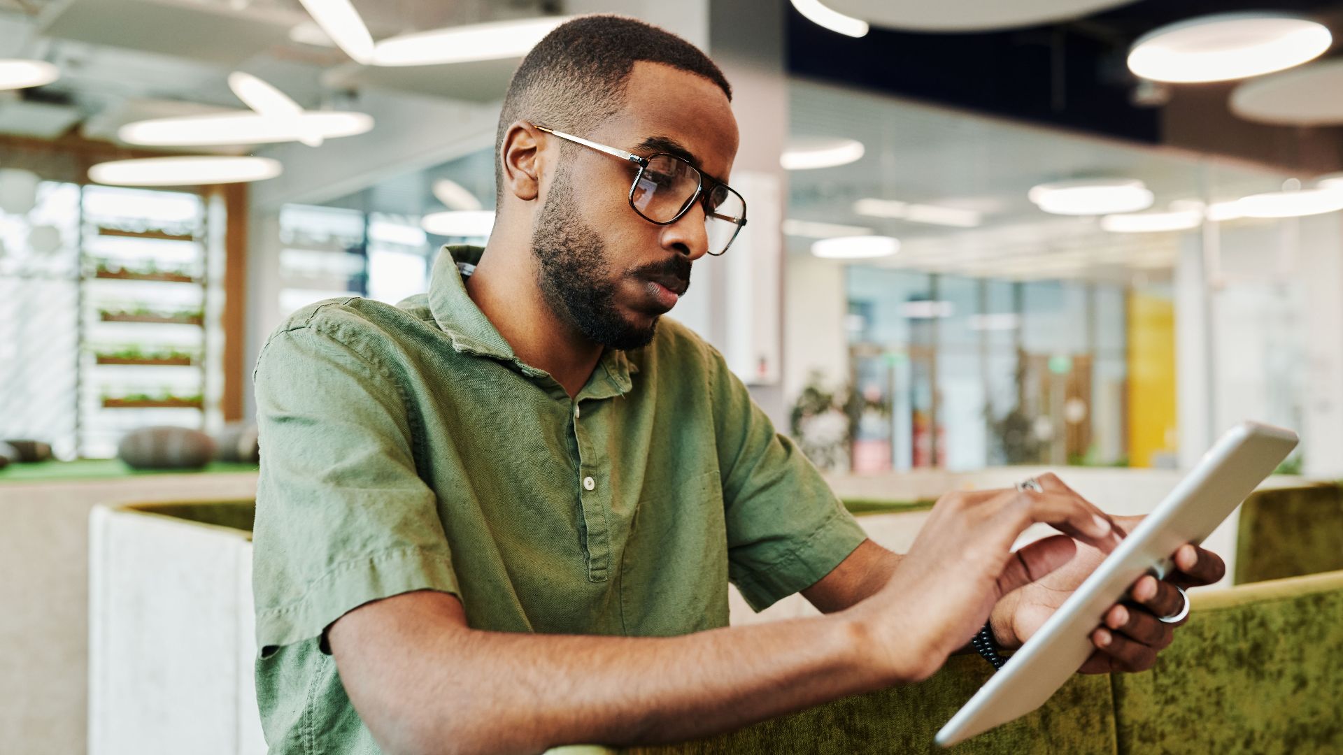 Man using a tablet in a modern office environment, concentrating on work.