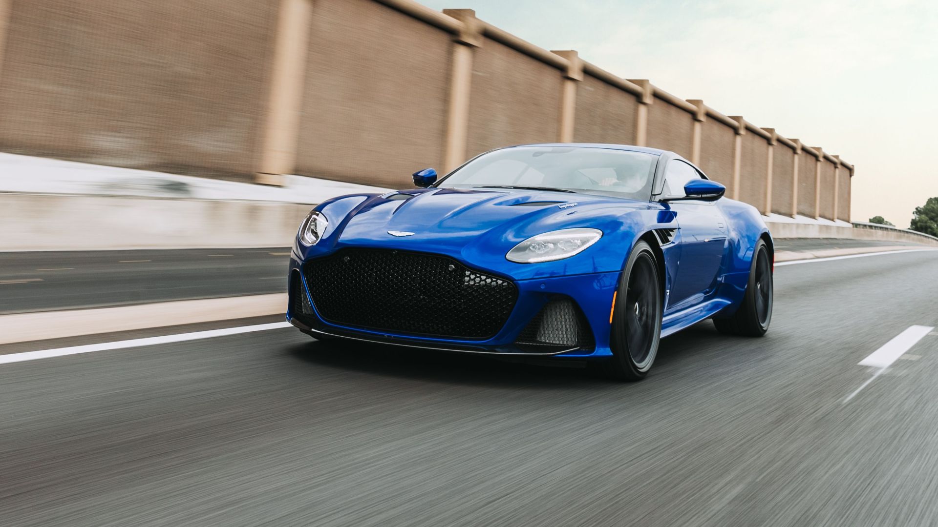 Luxurious blue sport car going fast on road in city district during sunrise
