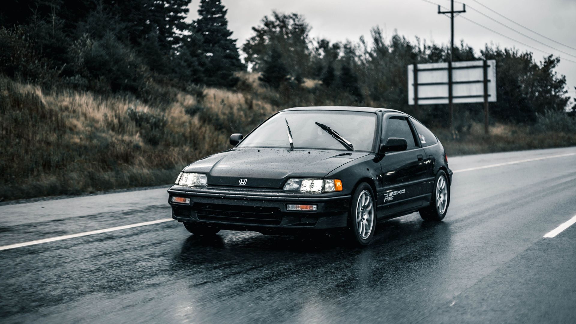 Black Honda car driving on wet road during rain, showcasing transportation in action.