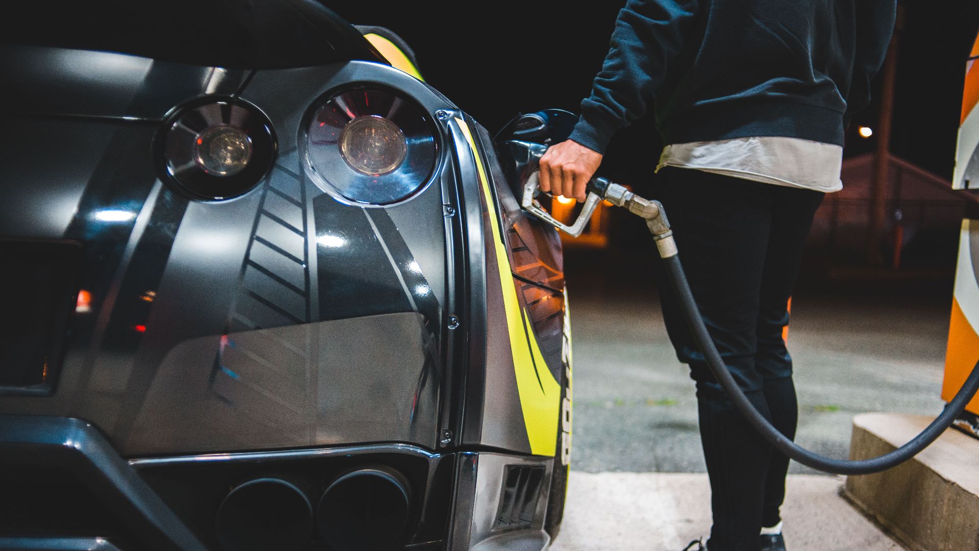 Side view of crop unrecognizable male refueling modern racing automobile in petrol station in evening