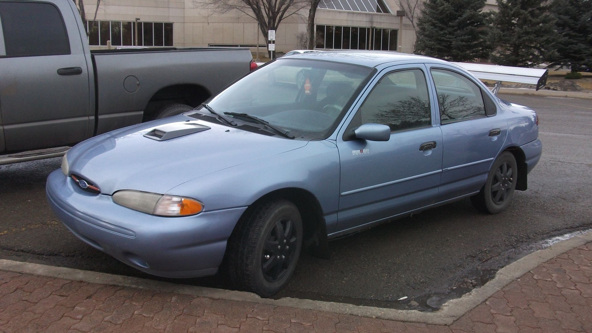 Ford Contour with huge wing, not so subtle hood blister and those of so fake looking, pretend alloy hub caps.