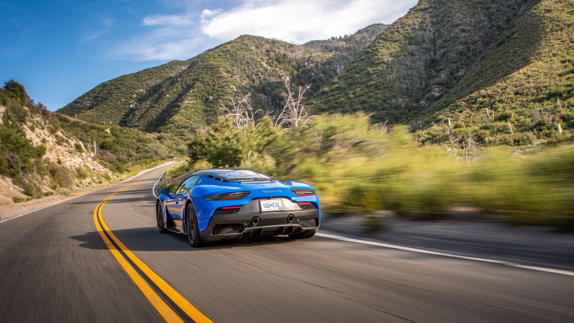 A sleek blue sports car speeds along a winding mountain road under a clear sky in Los Angeles.