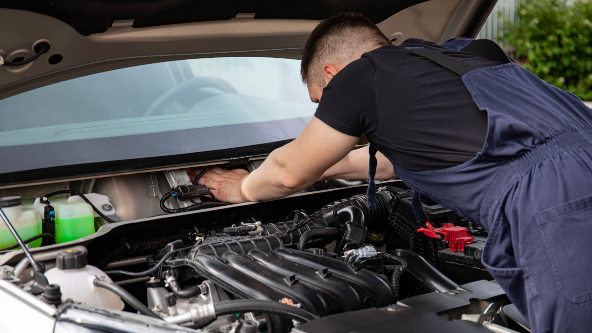 Auto mechanic performs engine maintenance on a car. Focus on hands and engine components.