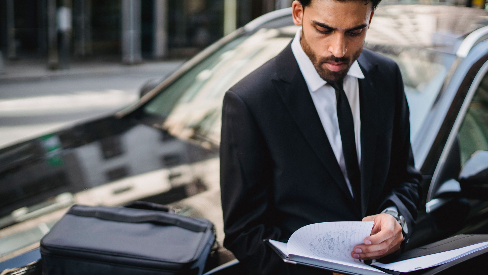 Confident businessman reviewing documents on the street beside a car.