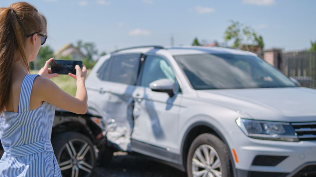 Stressed driver taking picture on sellphone camera of smashed vehicle calling for emergency service help after car accident. Road safety and insurance concept