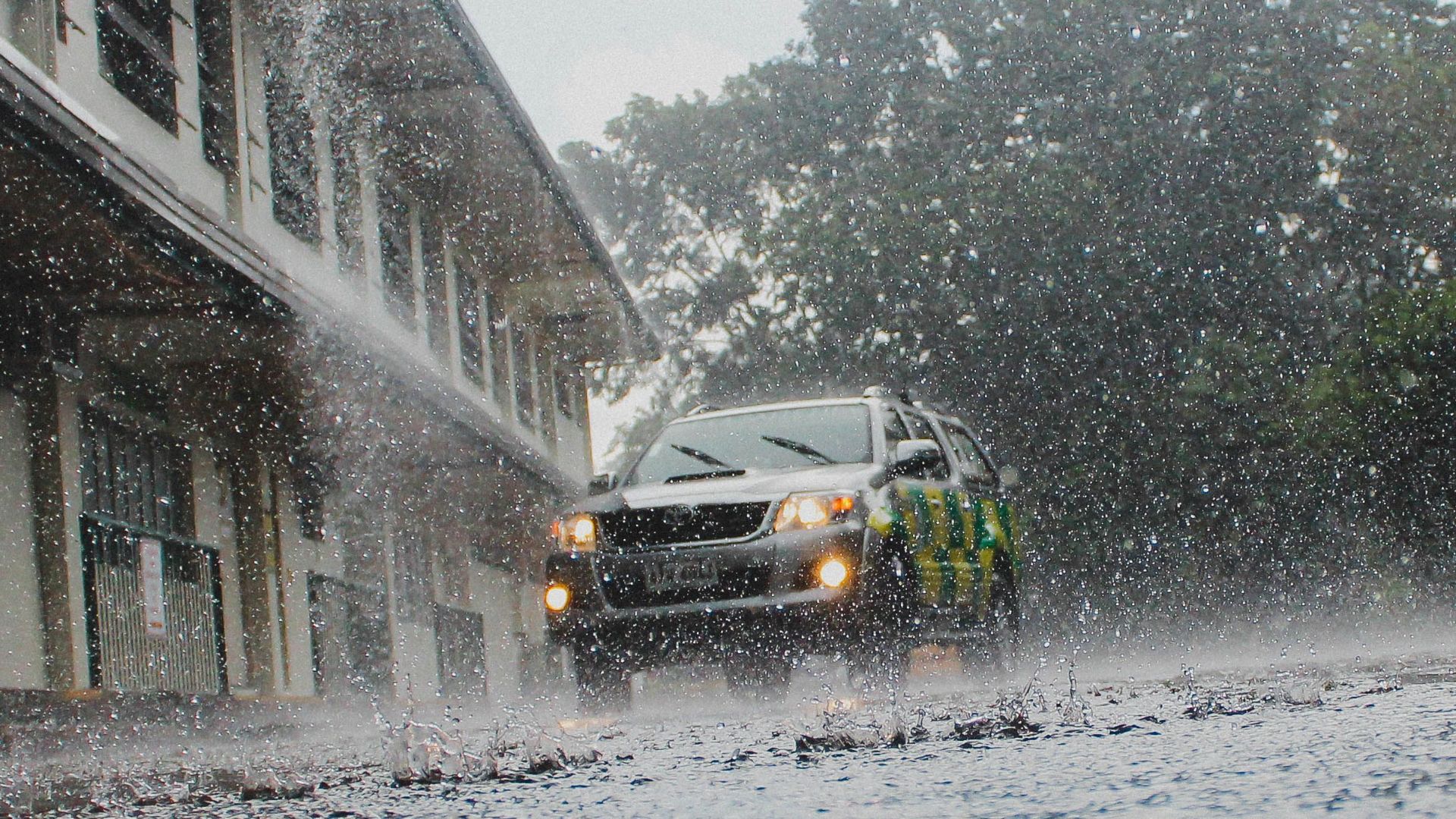 A car navigates a flooded street amid heavy rain and stormy weather.