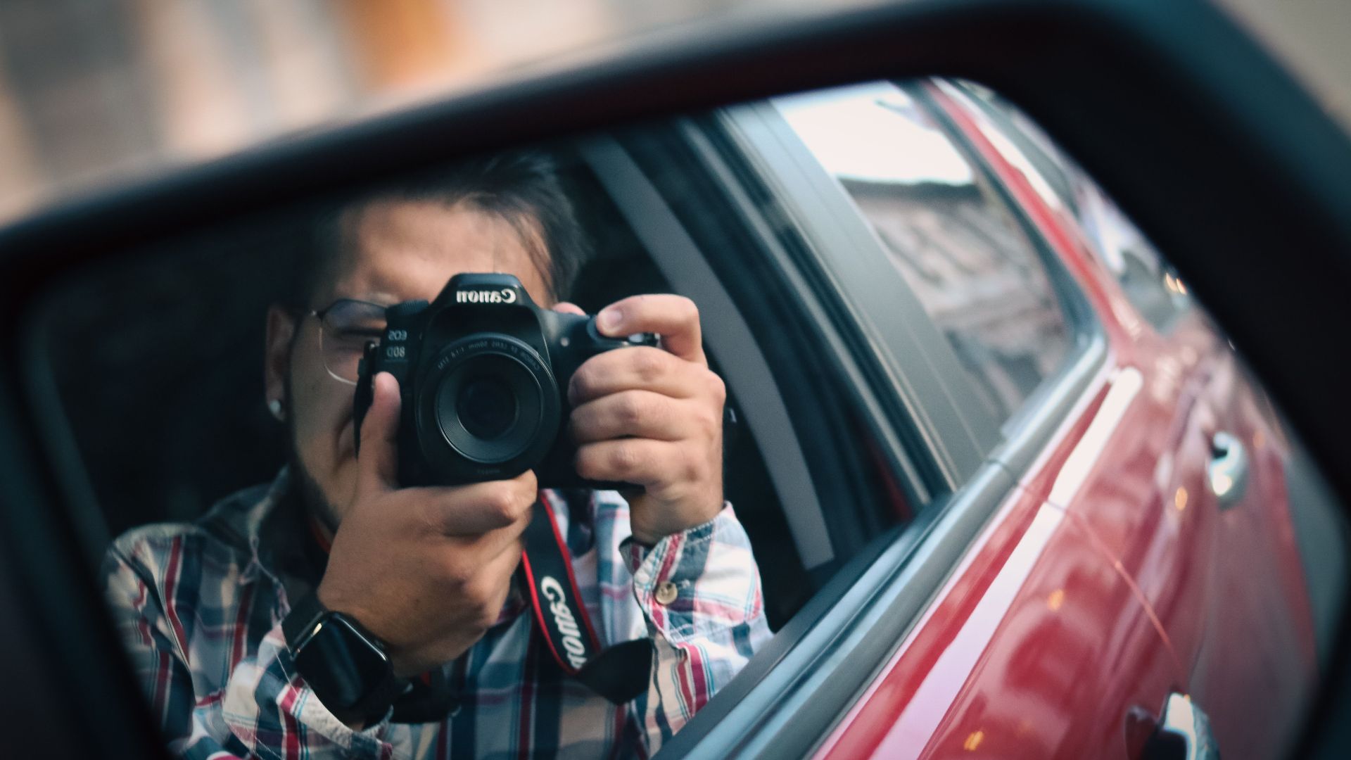 Close-up reflection of a photographer in a car mirror, capturing a unique perspective.