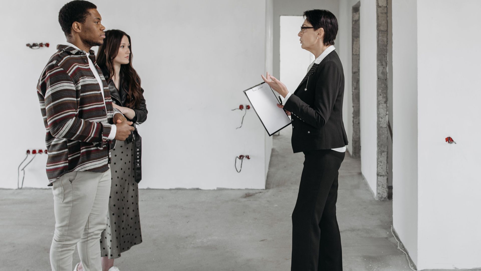 Real estate agent showing a house to a couple in a newly built home interior.