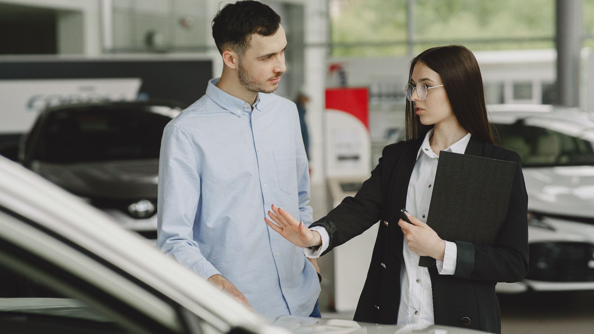 A salesperson and customer discussing car features in a dealership setting.