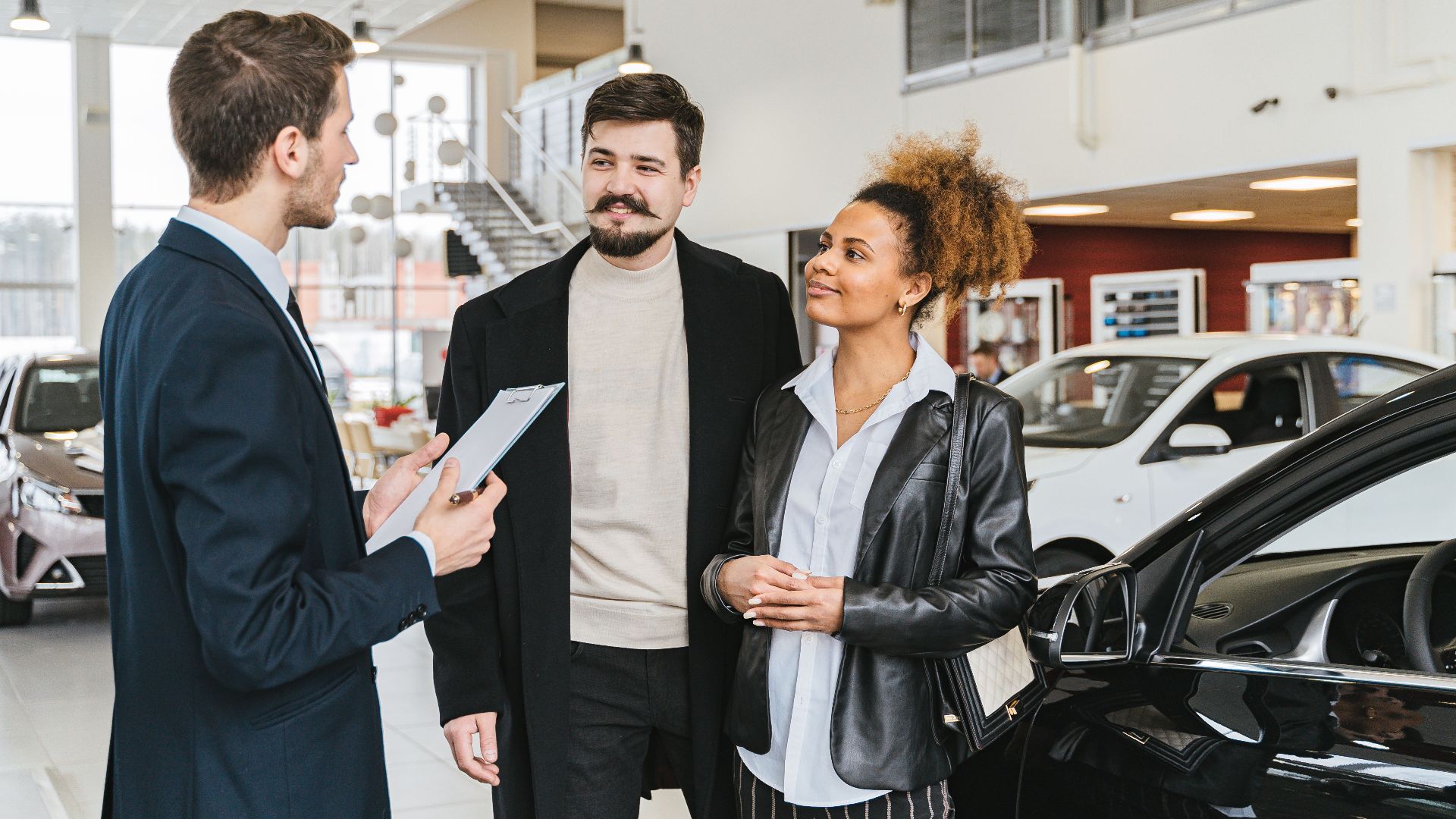 Couple discussing car purchase with salesman at indoor dealership, engaging conversation.
