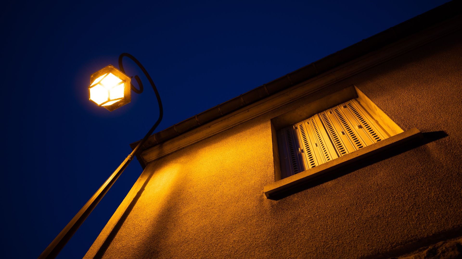Warmly lit streetlamp and window in Compiègne, capturing the architecture under a deep blue night sky.