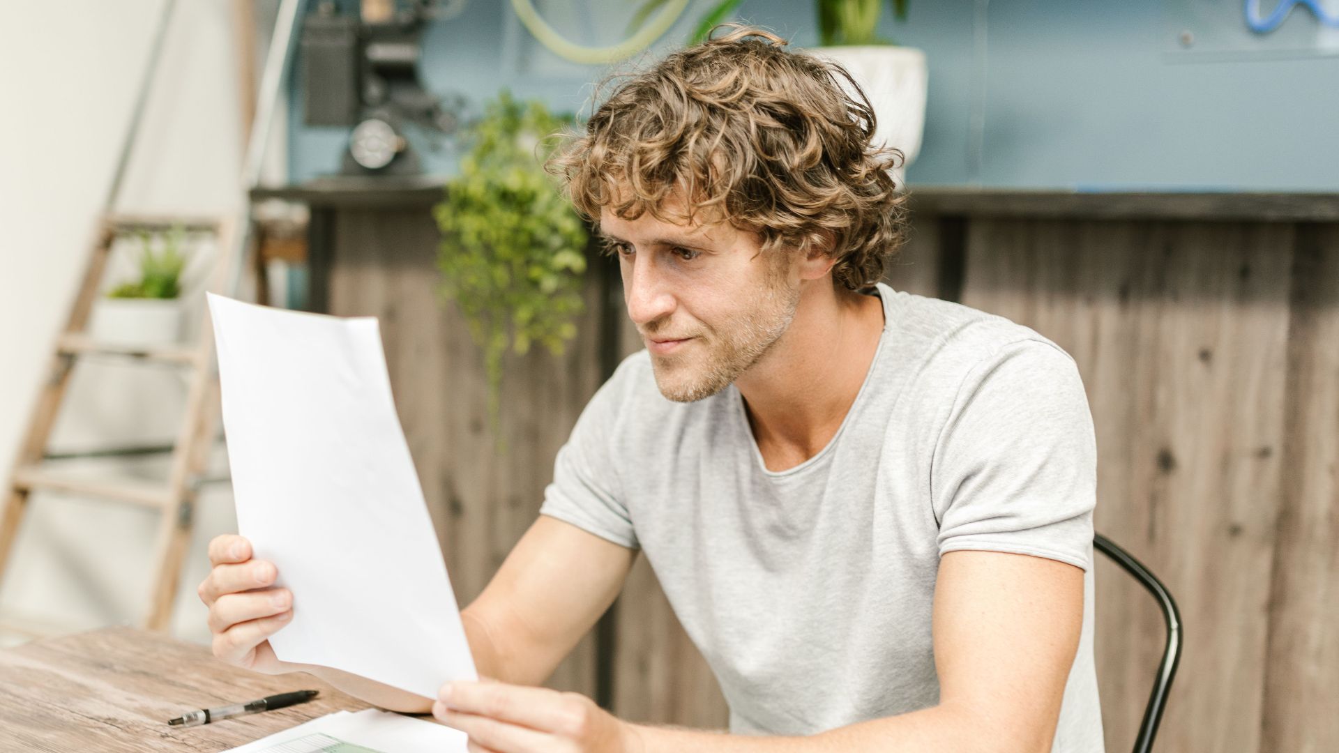 A man with curly hair evaluates documents at a desk, highlighting focused work in a professional setting.