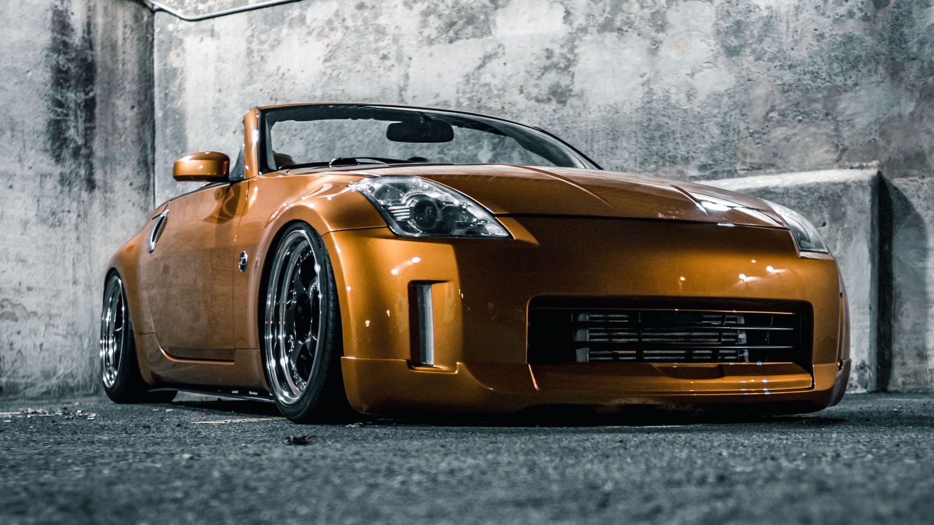 Ground level of bright modern sports automobile parked on asphalt pavement near shabby cement wall in evening