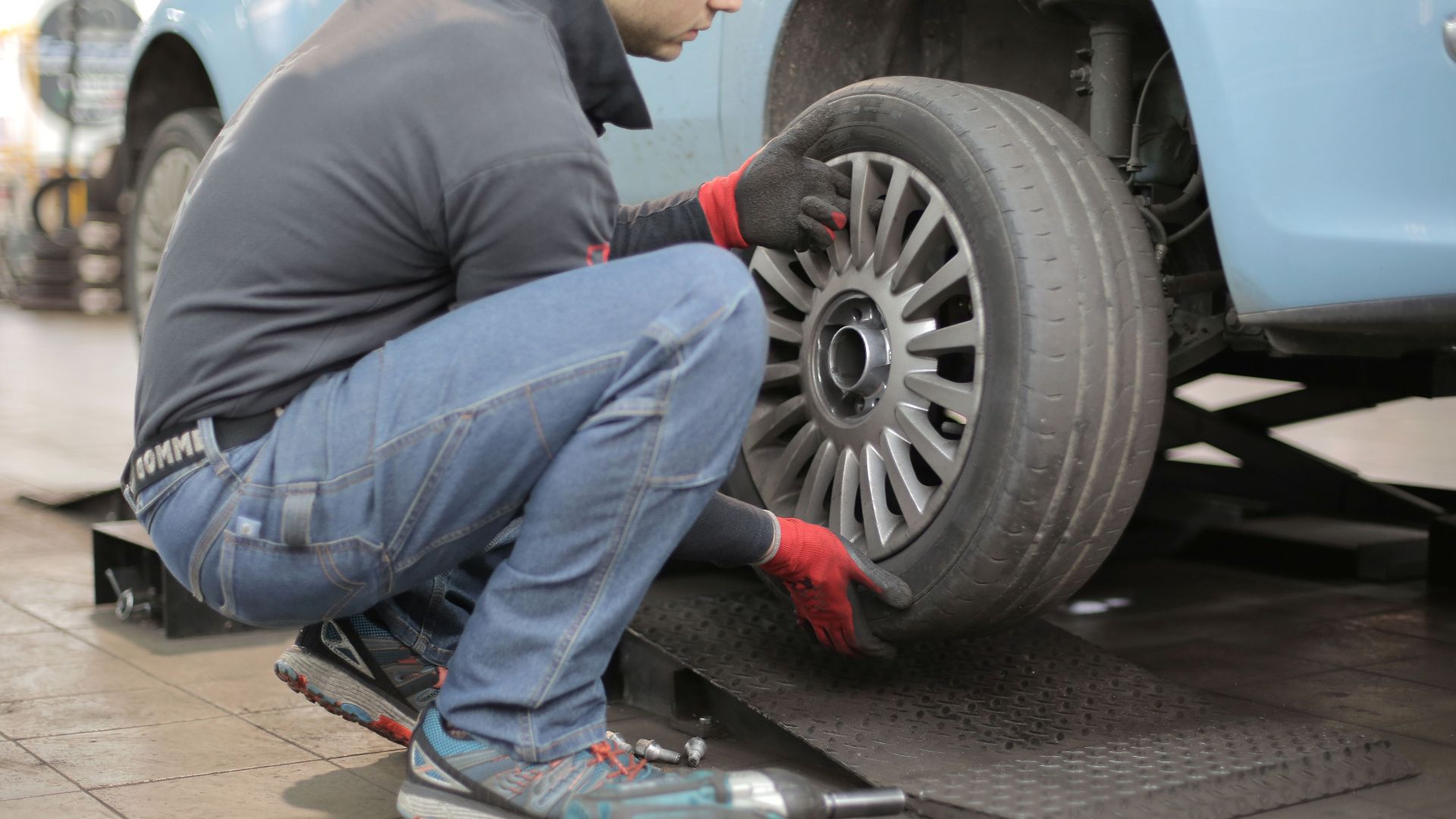 Mechanic changing a car tire indoors, using tools for vehicle maintenance.