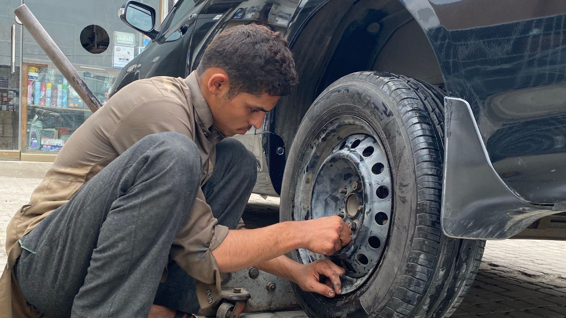 Mechanic crouched fixing a tire outdoors, showcasing vehicle maintenance.