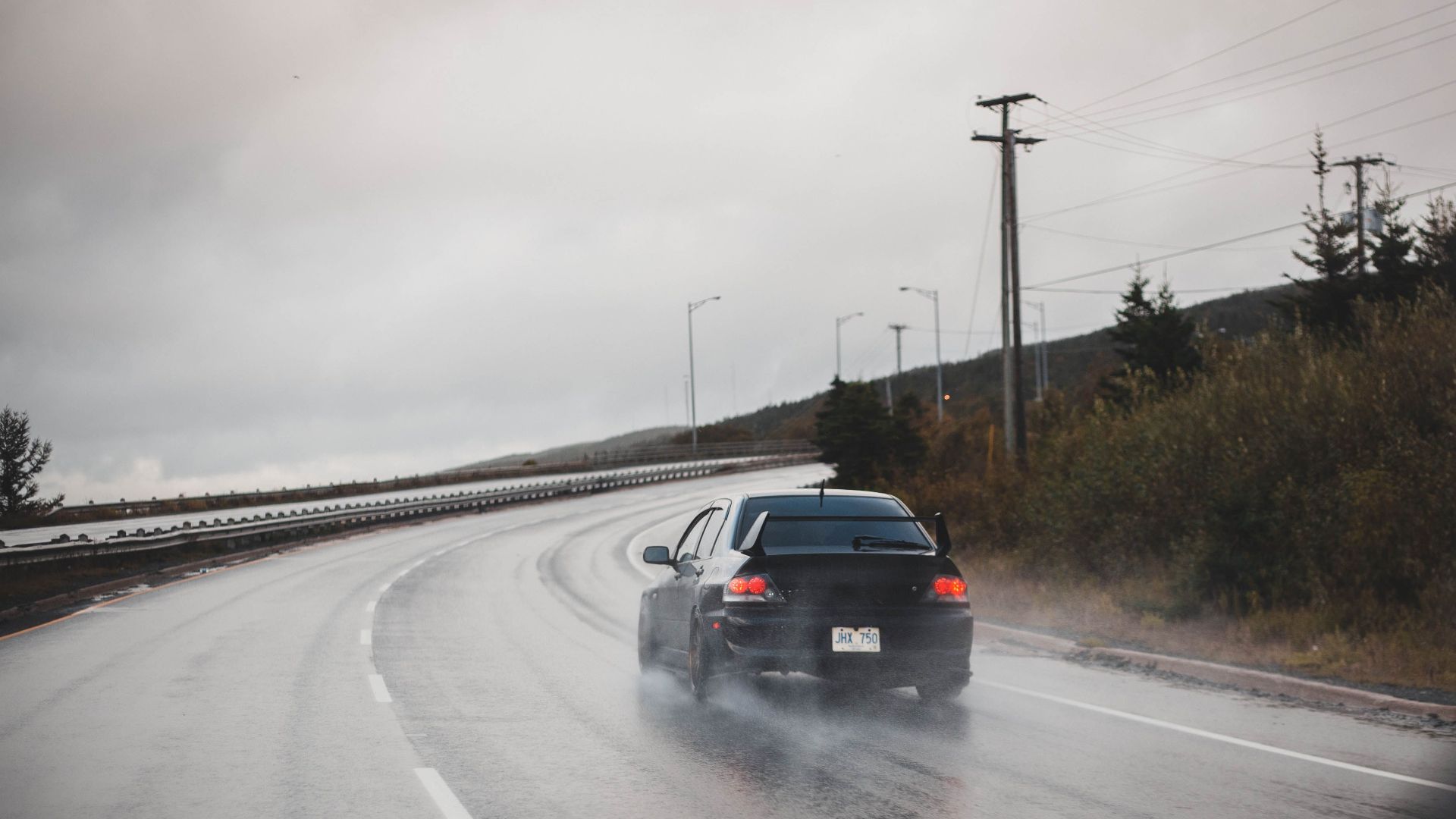 A black car drives on a rainy highway, showcasing speed and transportation.