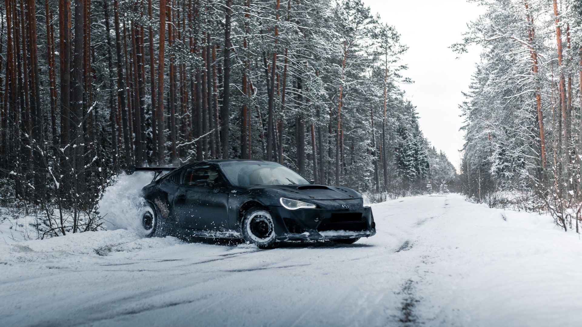 A sleek sports car drifting on a snowy road through a winter forest landscape.