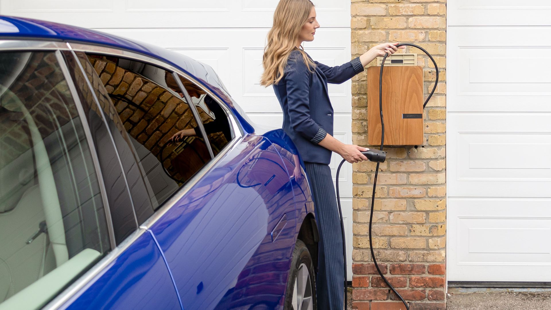 A woman efficiently charges her blue electric car at a home EV charging station.