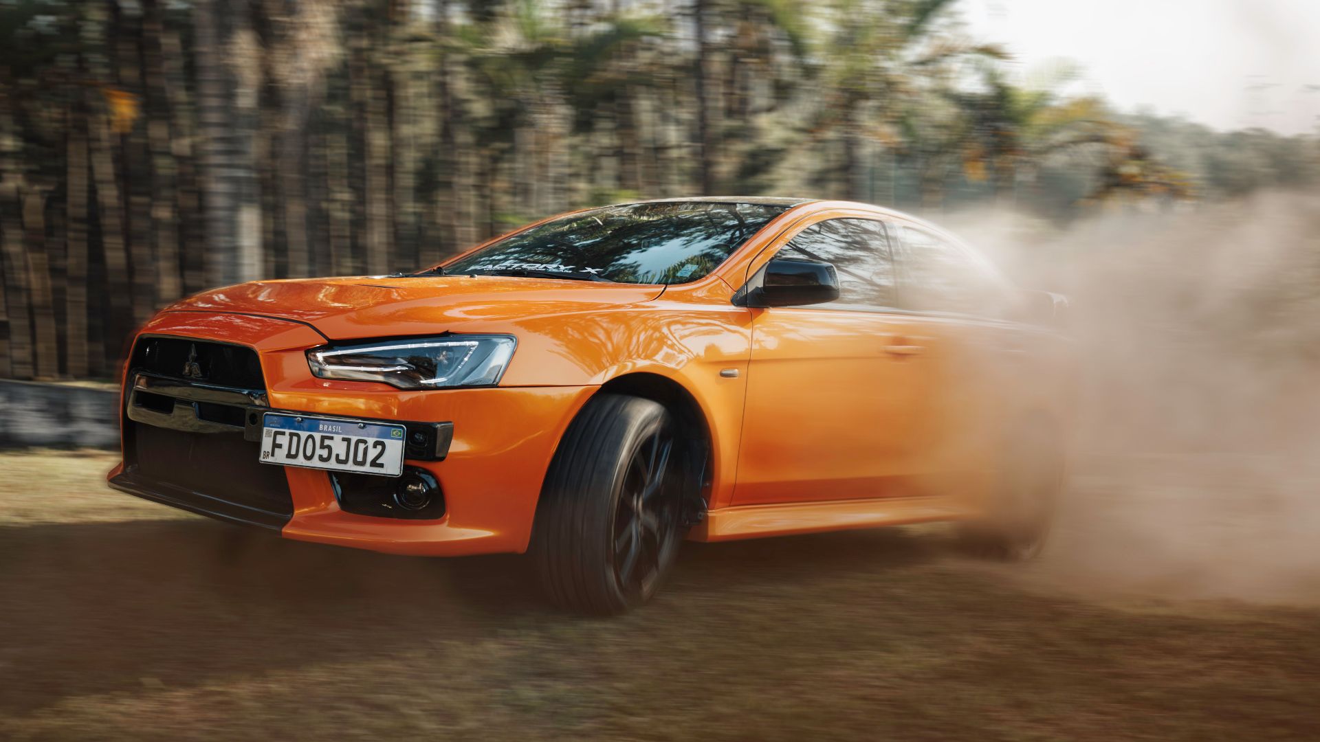 Orange sports car zooms through a dusty track, showcasing speed and power.