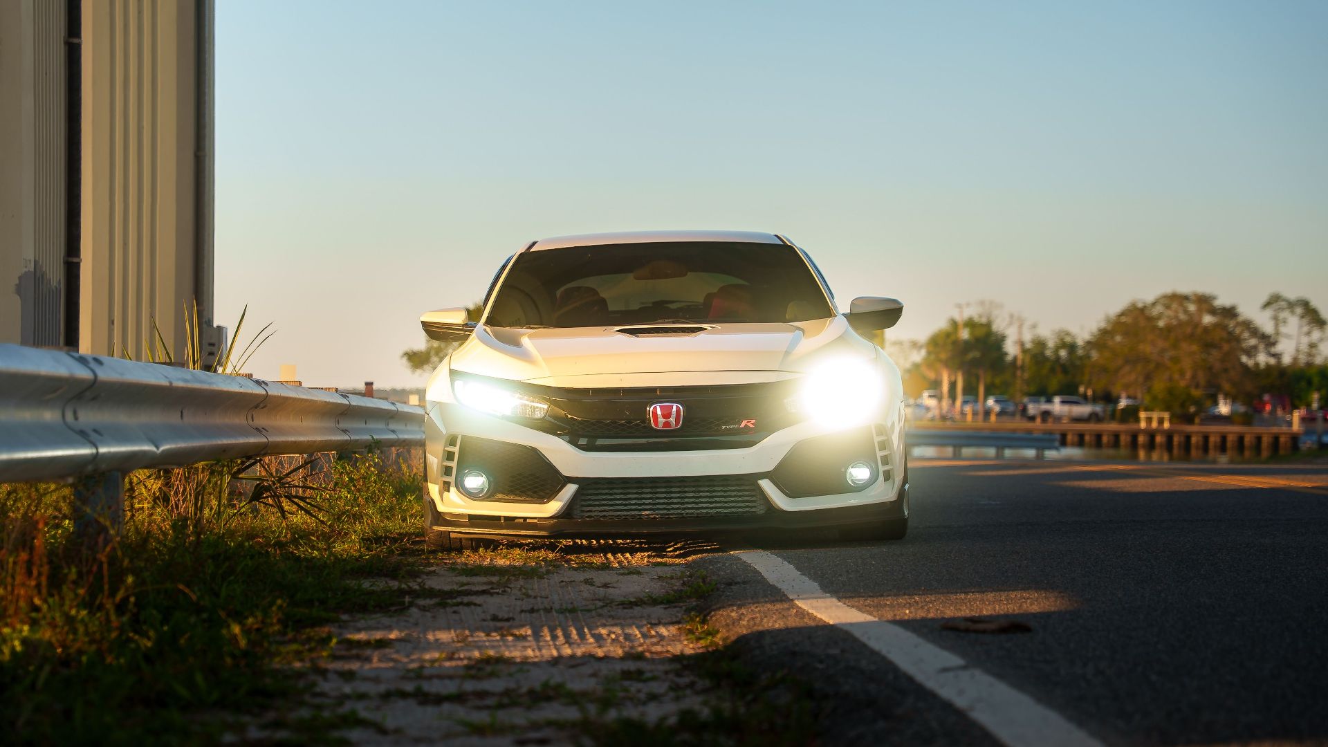 A sleek white car with headlights on, parked along a scenic highway at sunset.