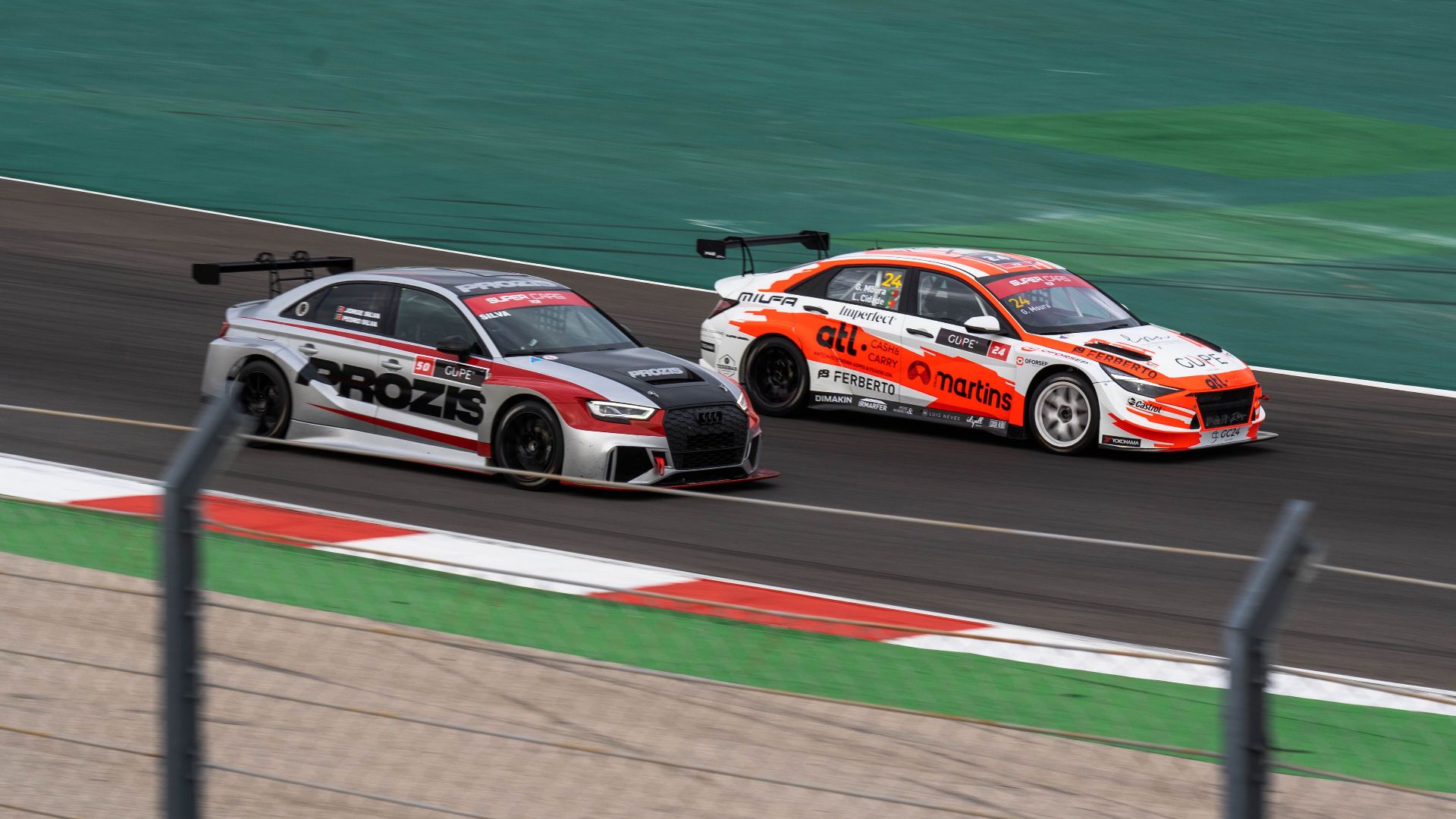 Two racecars compete at high speed on a professional race track, showcasing thrilling motorsport action.