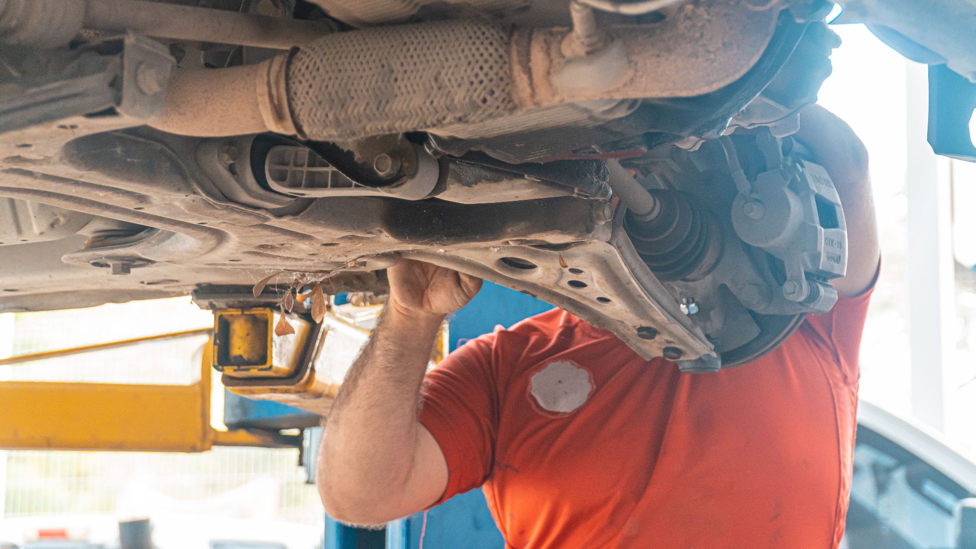 Mechanic working under a vehicle, inspecting the undercarriage in a repair garage, ensuring safety and performance.